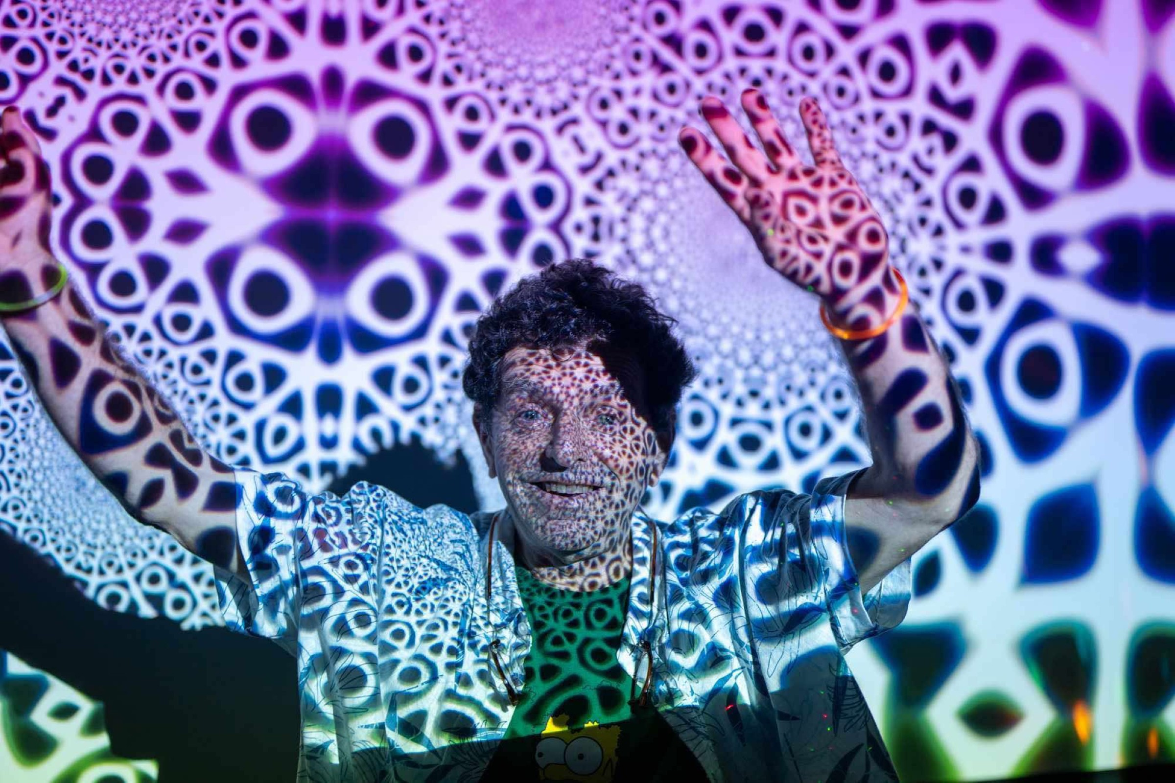 Man with arms raised has black and white projected on him and the screen behind him